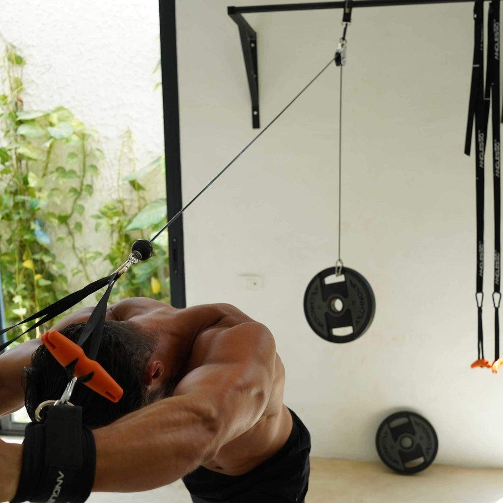 Man performing cable pulldowns in a home gym setting, using A90 Ankle Straps.