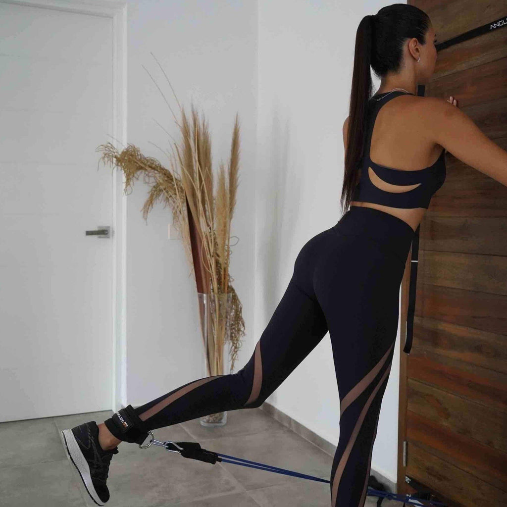 A focused individual in sportswear engaging in a resistance band workout at home, incorporating A90 Ankle Straps for a leg curl substitution.