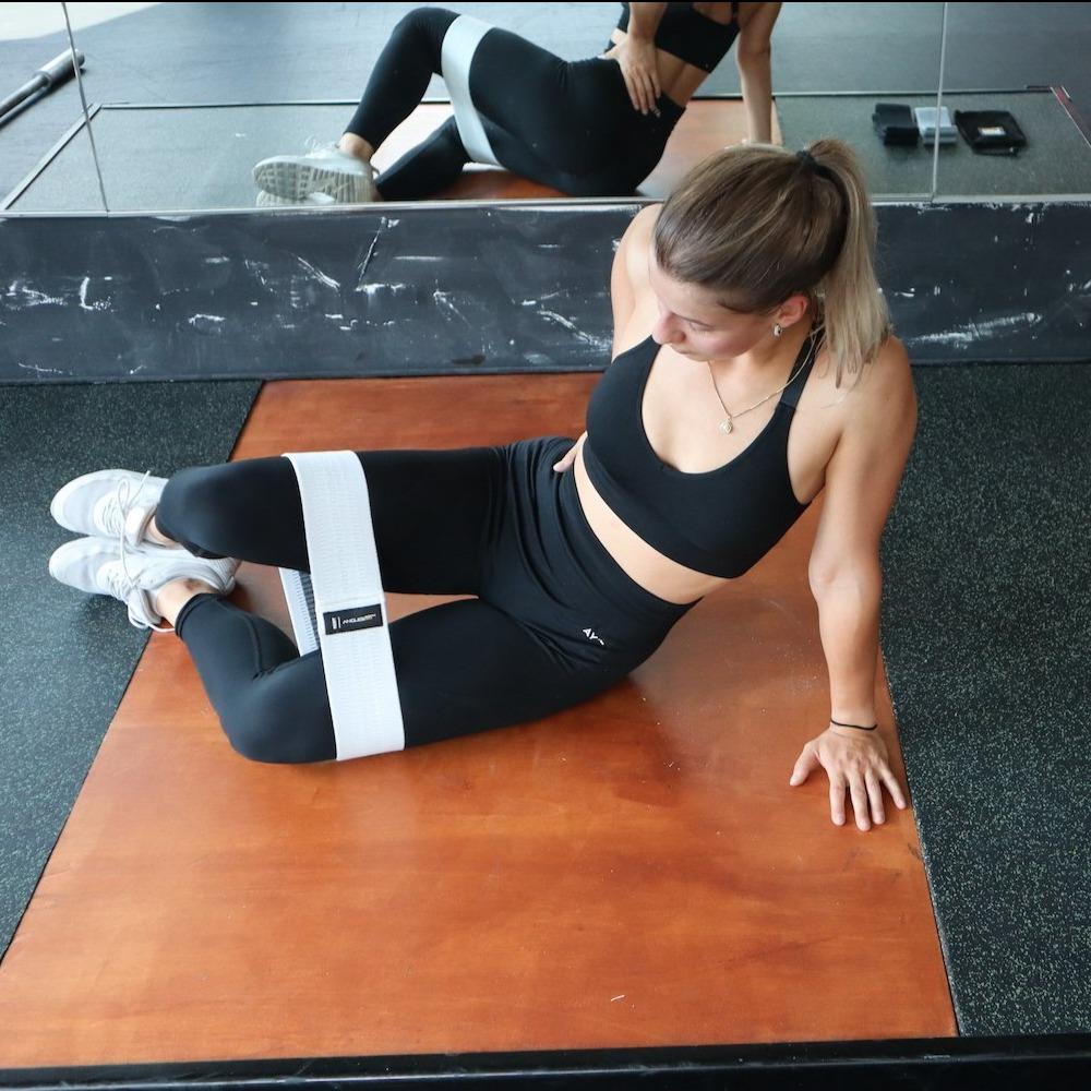 Woman in athletic wear using the A90 Leg Day Set with ankle straps for her workout routine in a gym setting.